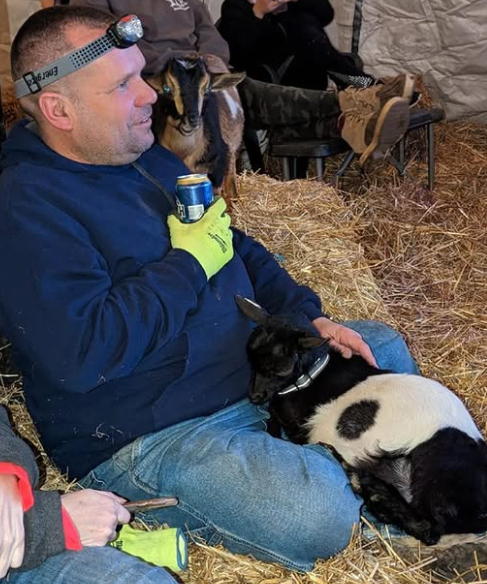 Jeff seated on hay with a black-and-white goat resting in his lap.