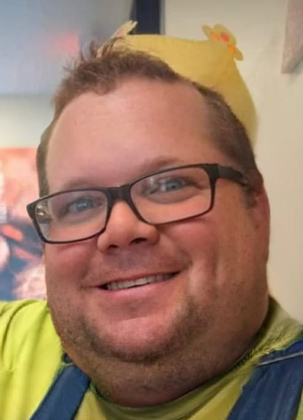 Jeff smiling in glasses and a yellow paper crown.
